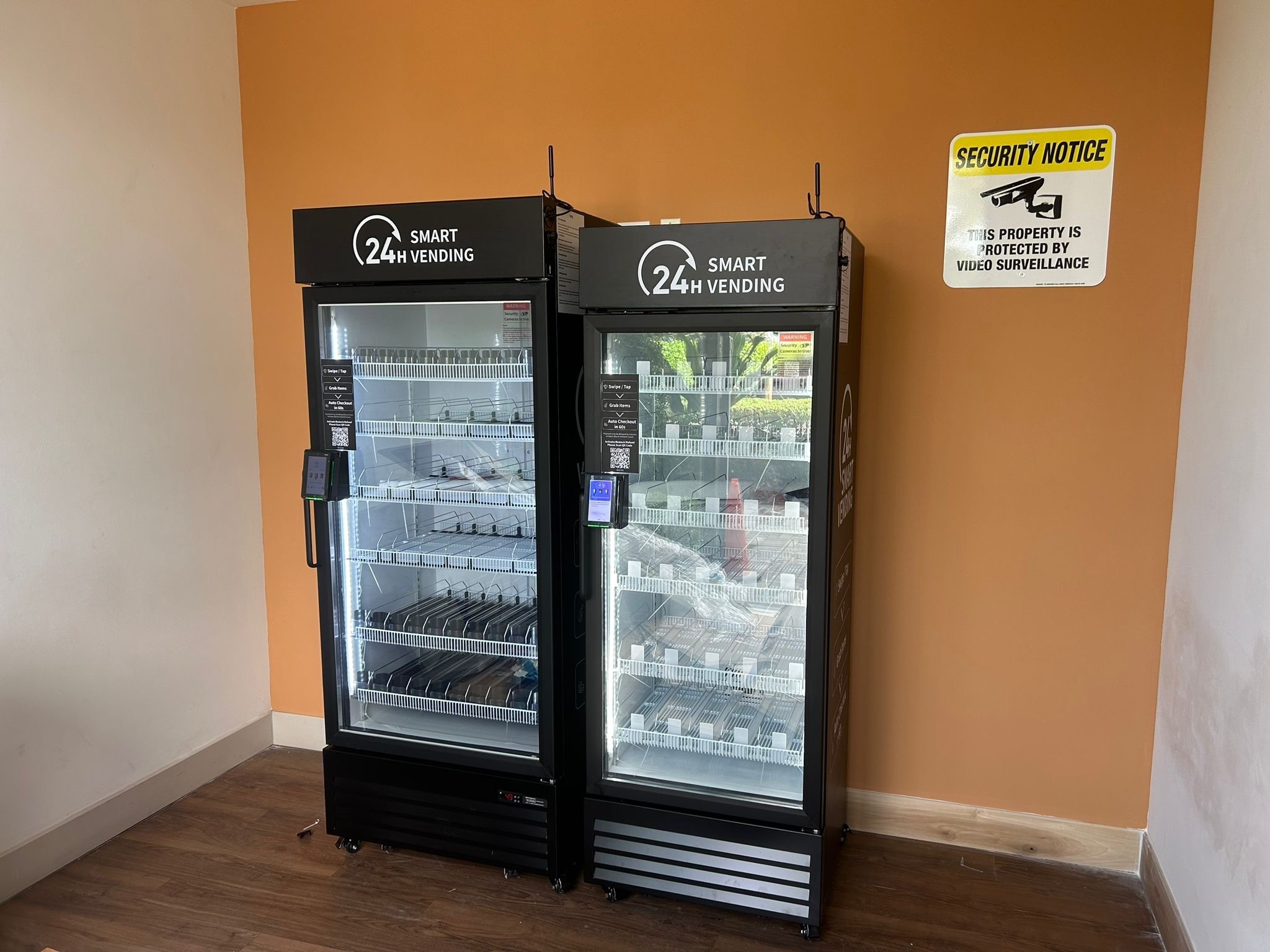 24-hour smart vending machines display an organized selection of products in a bright space, with a security notice on the wall nearby.